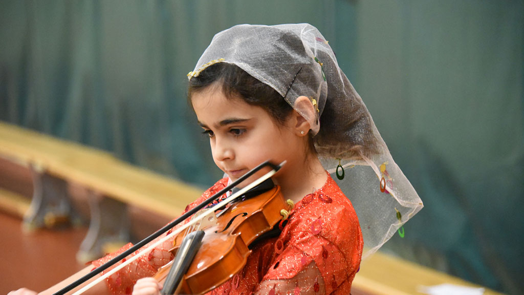 A Junior School student plays violin in traditional Persian attire