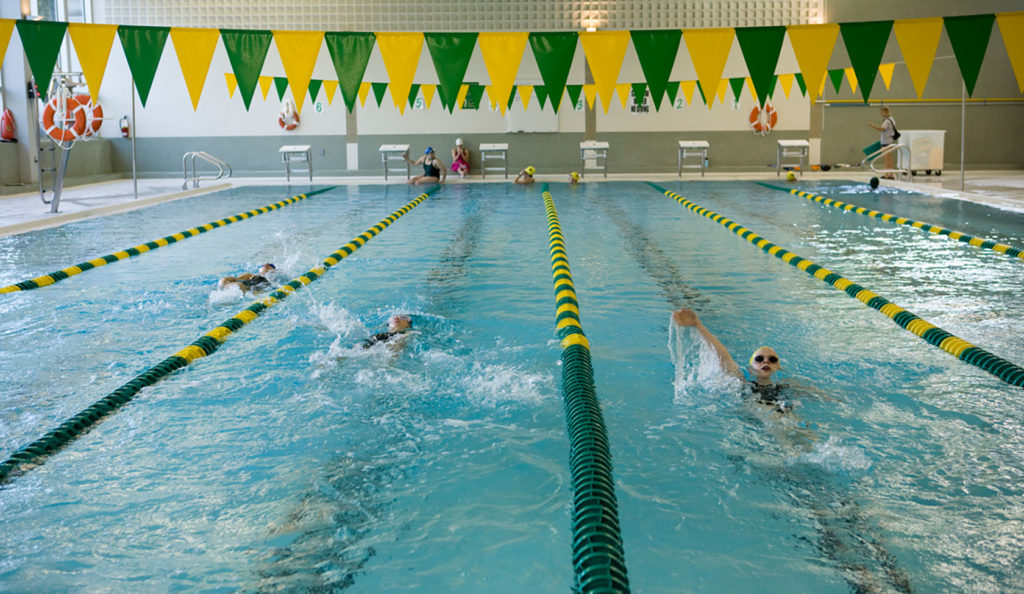 An indoor pool wiht swimmers and green and gold flags hanging above the pool.