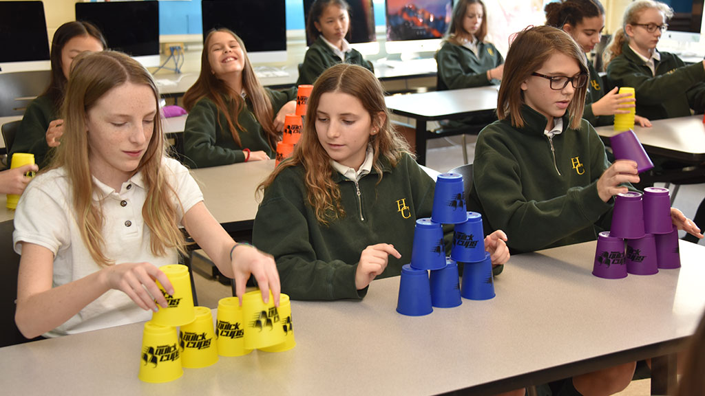 Three Middle School students stack coloured cups in their classroom.