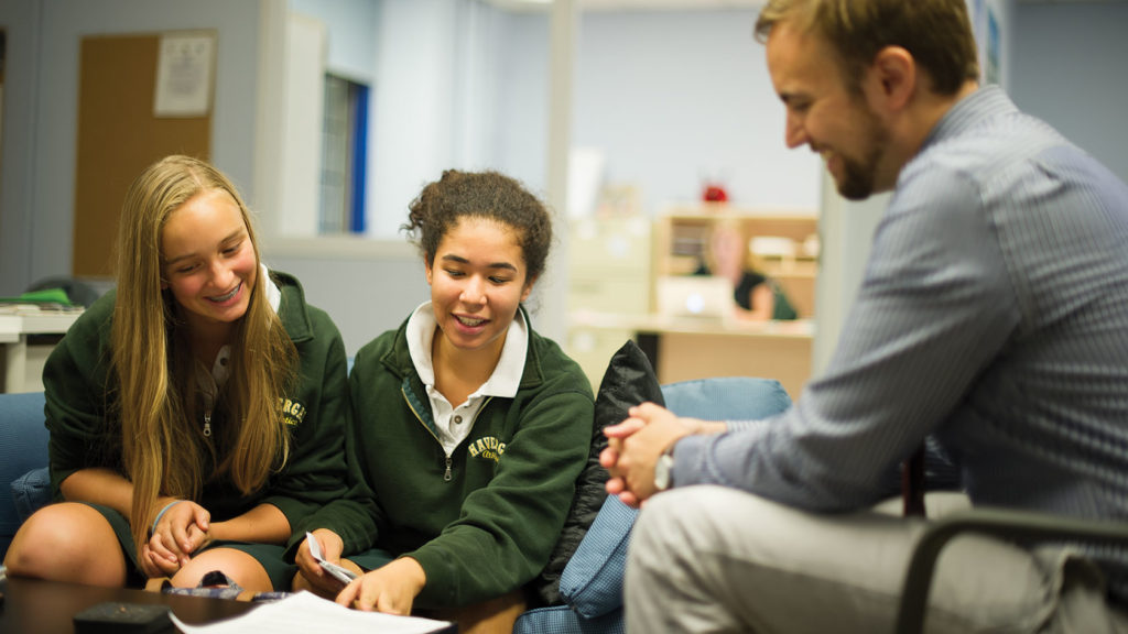 Two students discuss their work with a teacher.