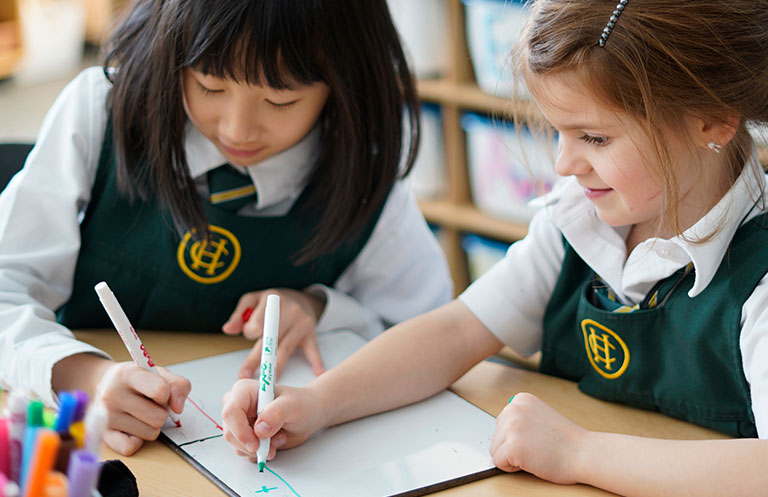 Two Kindergarten students draw together on a whiteboard