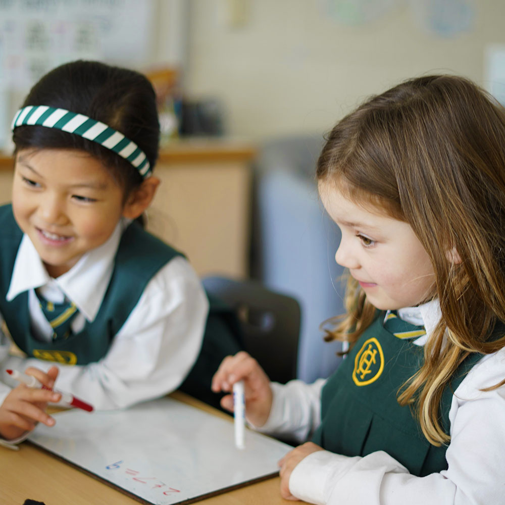 Two Kindergarten students completing a math equation on a white board.