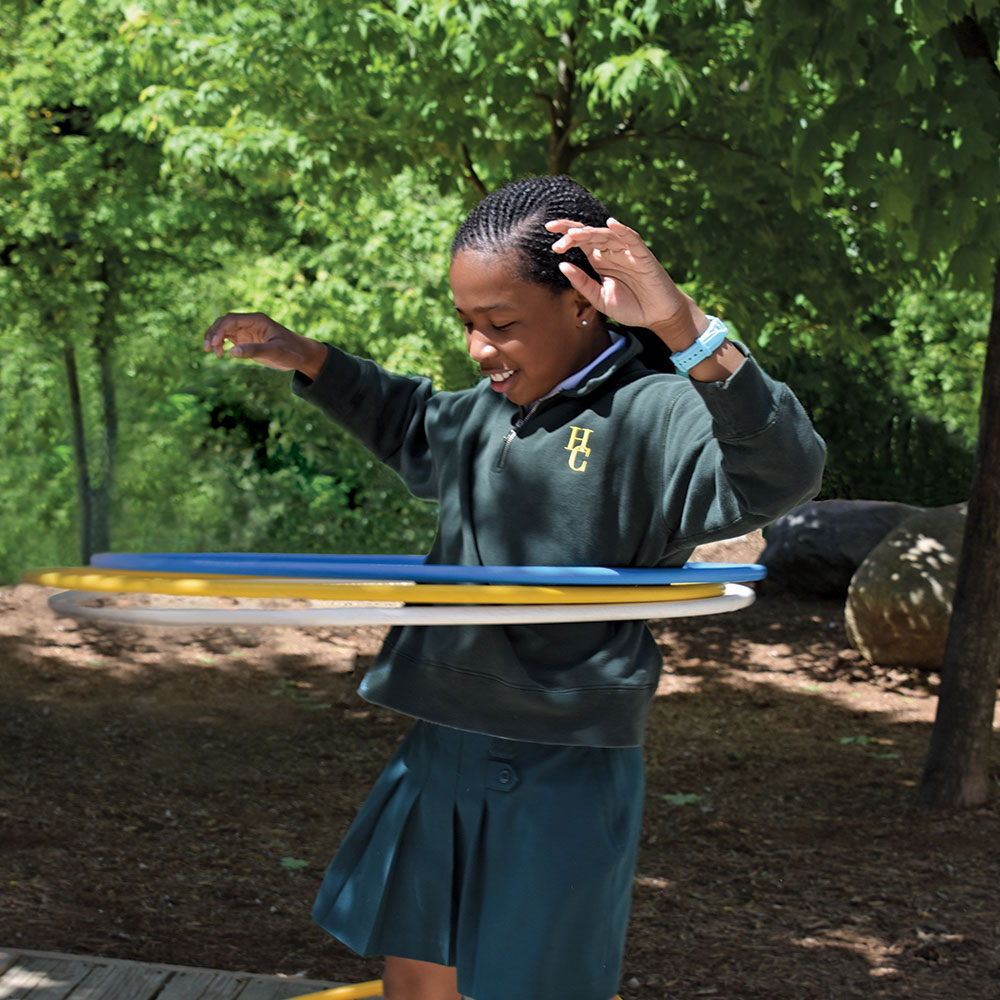 A Junior School student in a green sweatshirt hula hoops with three hoops.