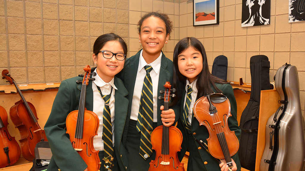 Three students pose together with their violins.