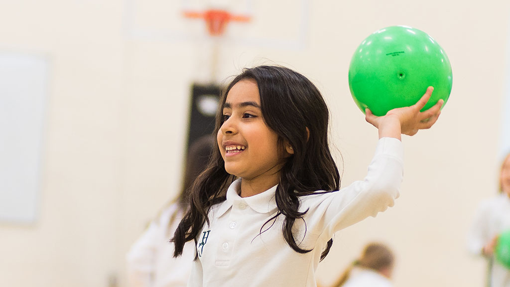 A Junior School student throws a green ball in the gym.
