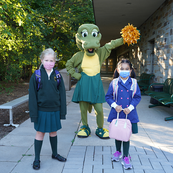 students standing outside of the school with the Gator mascot