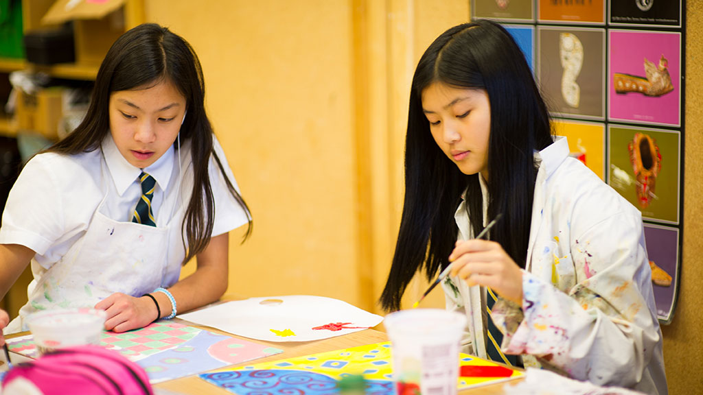 Two students sit at a table together while painting.