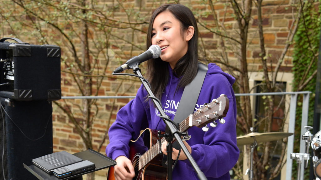 A student sings and plays guitar on an outdoor stage.