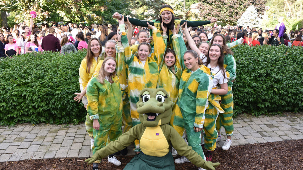 Prefects wearing green and gold spirit gear pose with the Havergator mascot.