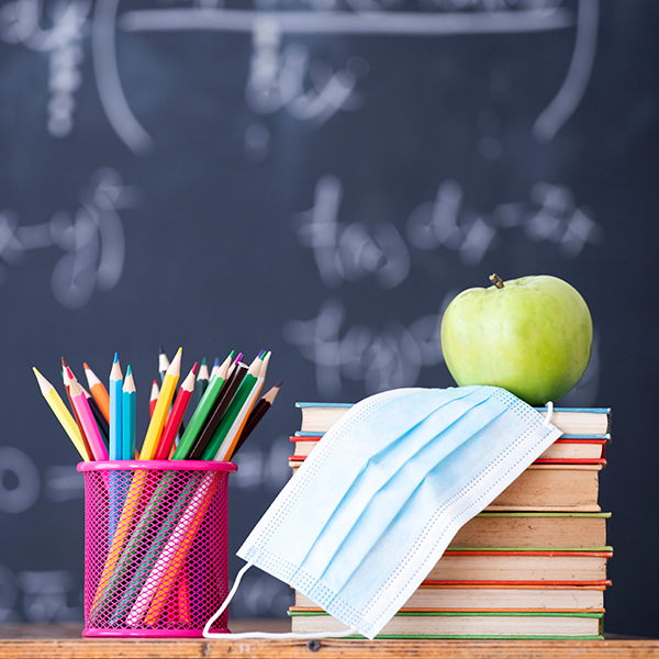 image of a desk with pencil crayons, a mask, an apple and textbooks