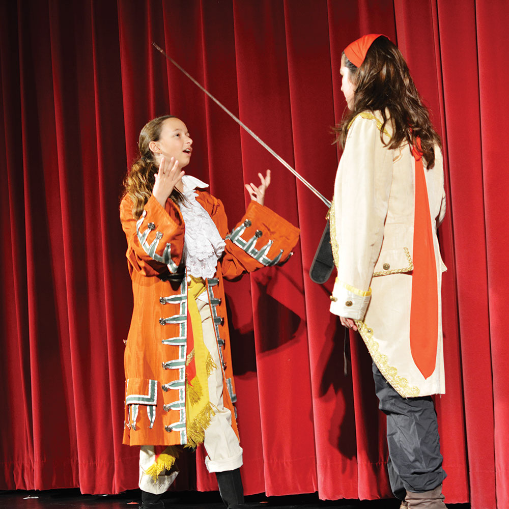 Two students act in front of a red velvet curtain wearing pirate costumes.