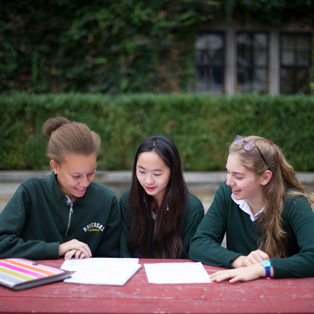 Three students sitting at a picnic table work on an assignment.