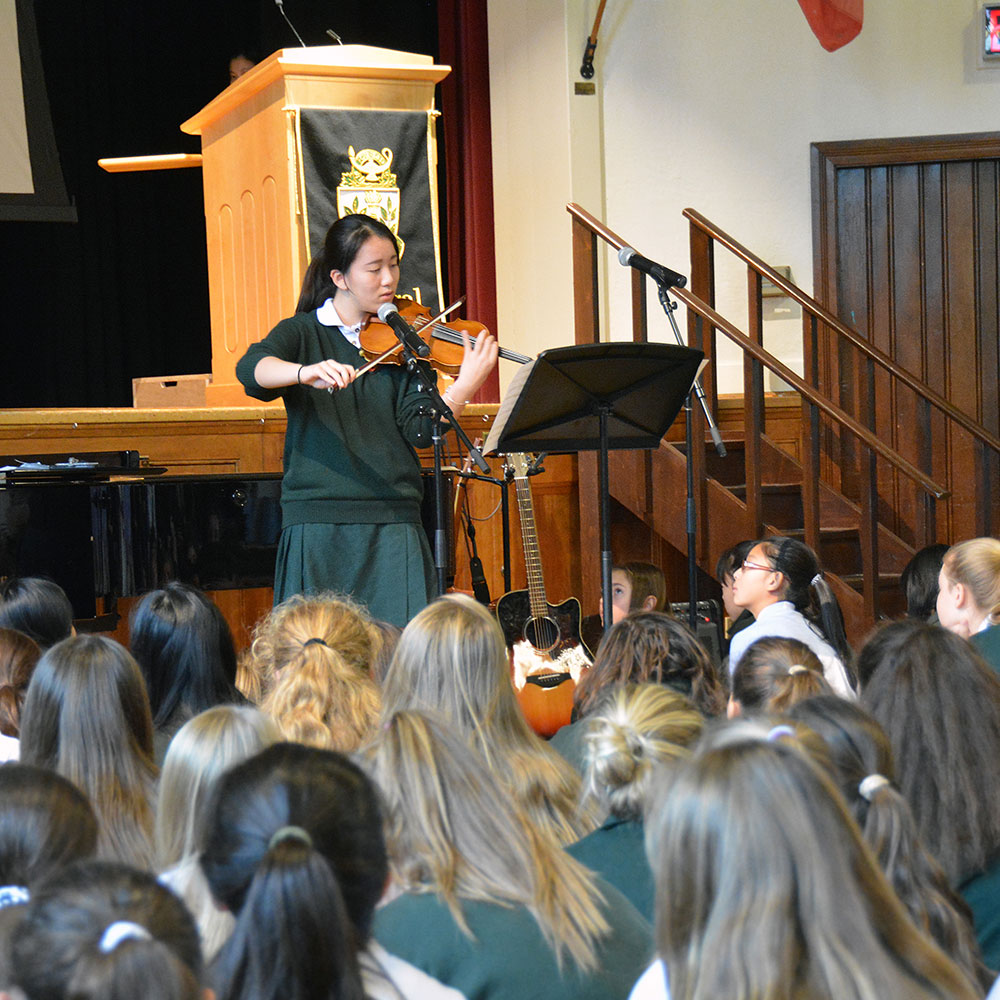 A student plays violin in front of a crowd in the Brenda Robson Hall.