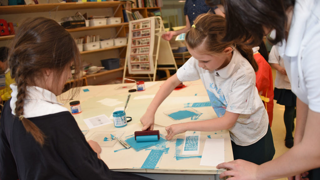 A Junior School student actively engaged in printmaking with light blue paint.