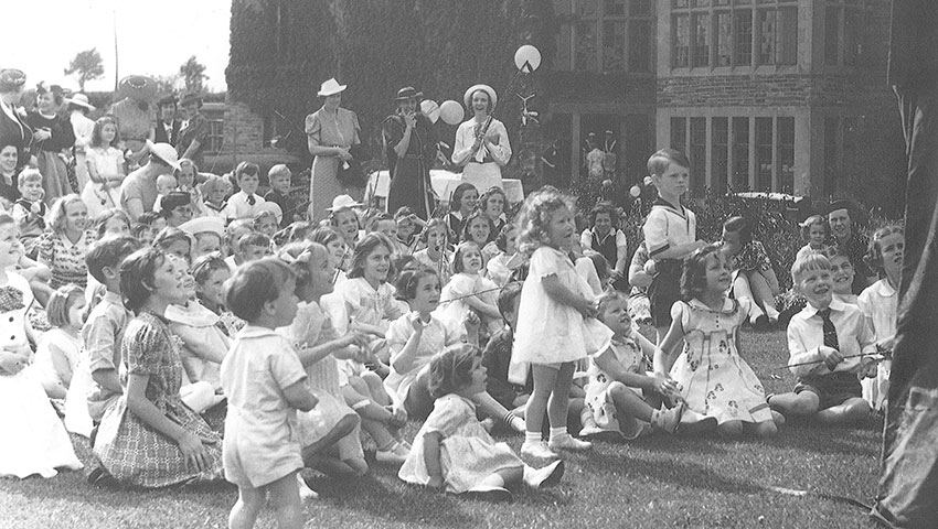 Black and white photo of young children sitting in the South Quad to watch a puppet show.