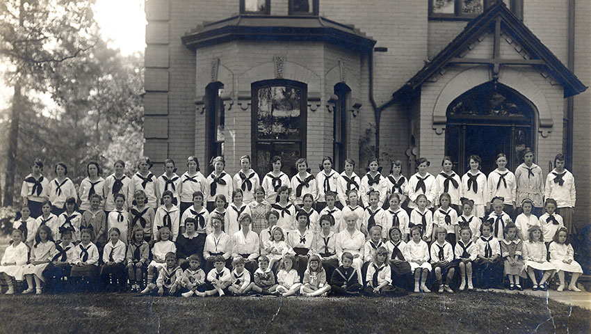 Black and white photo of students posing in front of a school wearing uniforms.