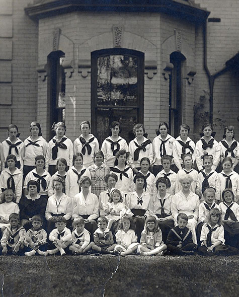 Black and white photo of students wearing a school uniform standing together in front of a building.