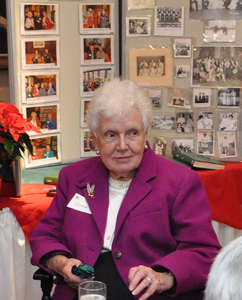 An elderly woman at a holiday event seated at a table.