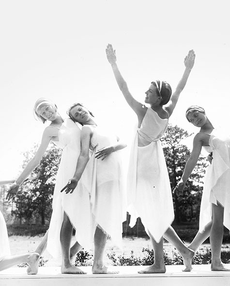 Black and white photo of students in white dresses performing a dance routine outdoors.