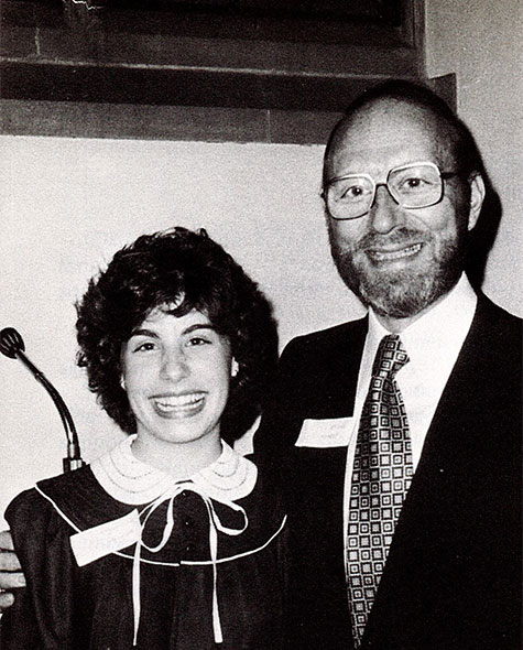 Black and white photo of a dad and a daughter standing beside each other while smiling.