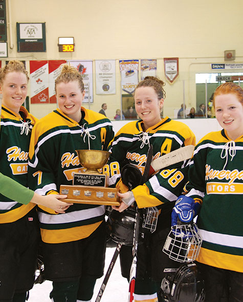 Four students in green and gold Havergal hockey jerseys hold the Hewett Cup.