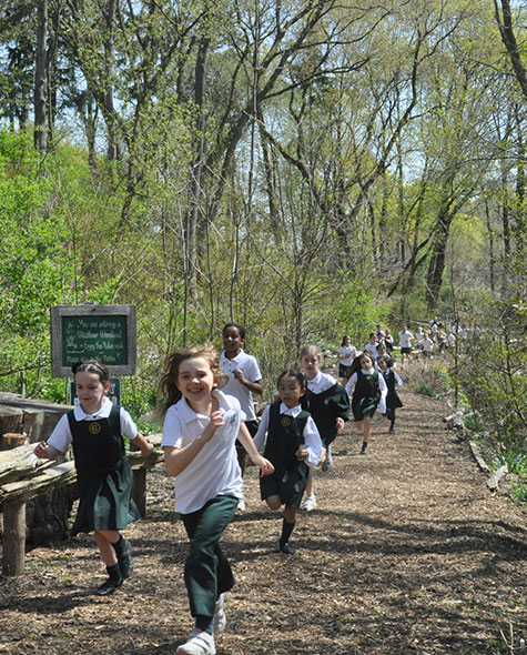 Junior School students in uniform run on a trail in a forest setting.