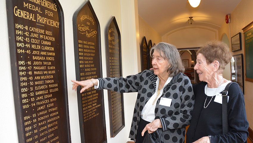 Two alumni look at a display in an Upper School hallway.