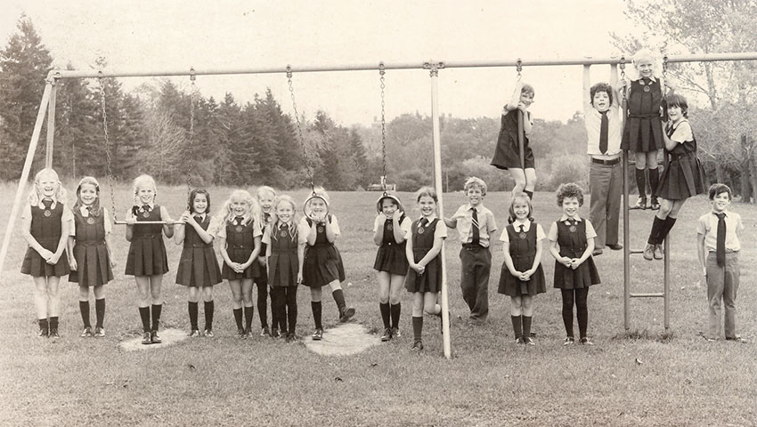 Black and white photo of girls and boys posing by a swingset.