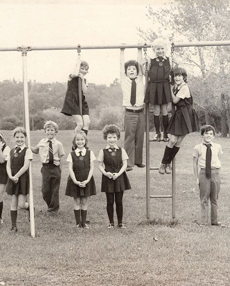 Black and white photo of young boys and girls in their school uniforms posing on and around a swing set.