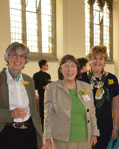 Three Cinquantenaires pose together in the Brenda Robson Hall with yellow daisies pinned to their shirts.