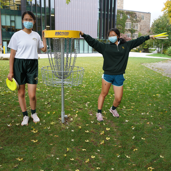 Students posing next to Disc Golf goal post