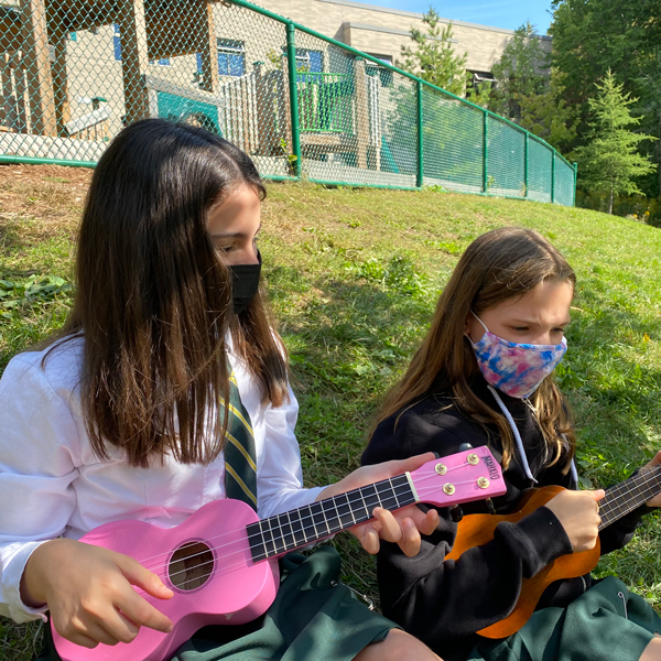 Junior School students playing ukuleles outside on a sunny day.