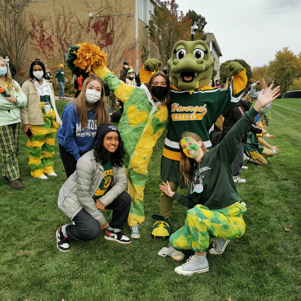 Students dressed in green and gold spirit wear posing with the Havergator