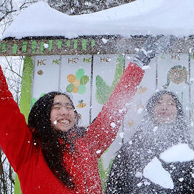 A Boarder throws snow in the air as another looks on.