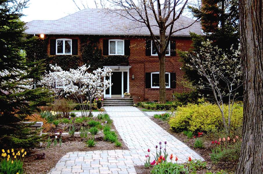 An older brick house with a well maintained brick path and gardens. 