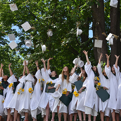 Students in white gowns throw graduation caps into the air.