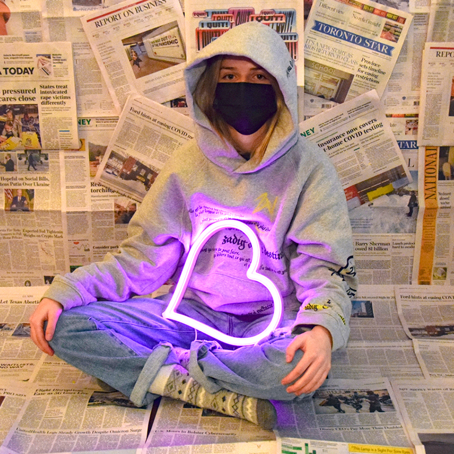 Student art of a student in a hoodie sitting around newspapers holding a neon heart.