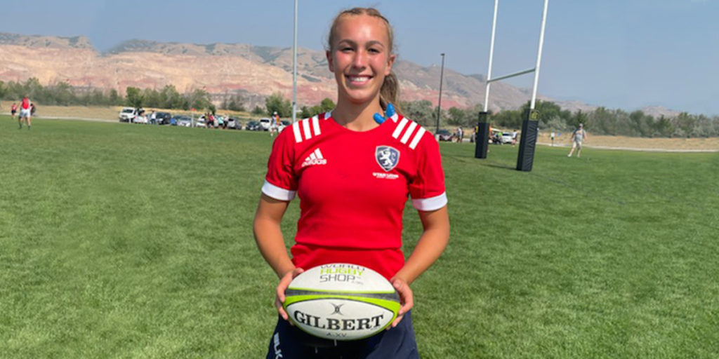 Victoria standing on a field in her rugby uniform holding a rugby ball.