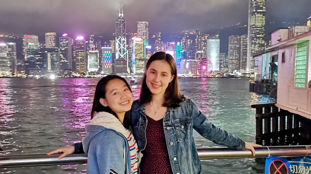 Two students pose together on a pier in Hong Kong at night.