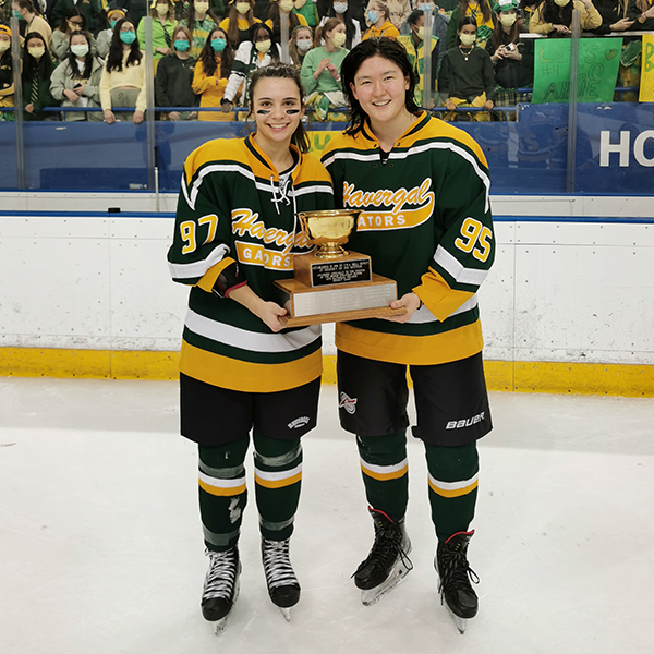 Piper and Beats in Hockey uniforms, on the ice, holding the Hewitt Memorial Cup
