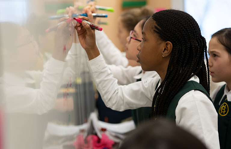 A Junior School student writes on a whiteboard with a pink marker.