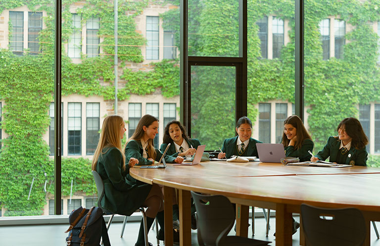 Six Upper School students sit around a Harkness table in a classroom.