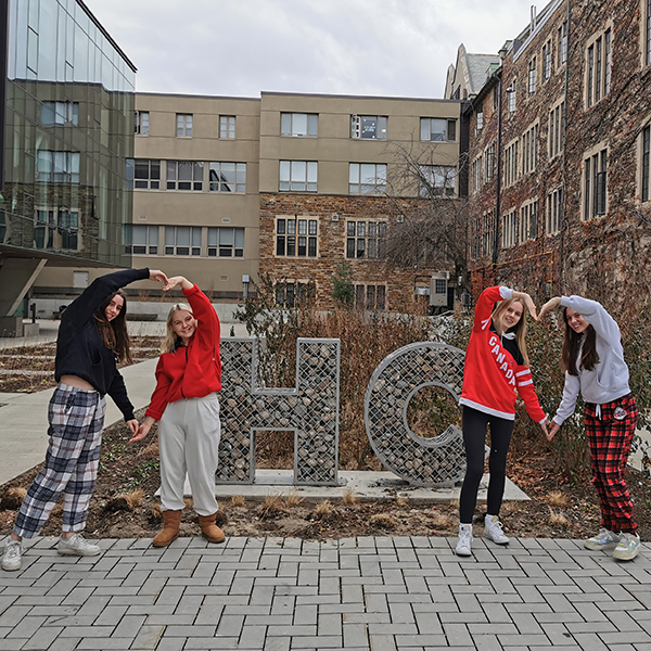 Students standing next to the HC Sign making heart shapes with their arms.