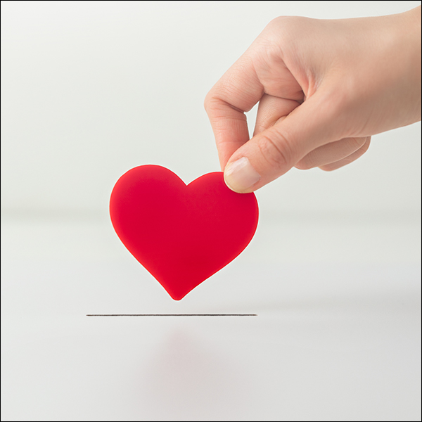 hand holding a heart and putting it in a slot, like a donation slot.