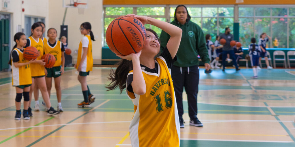 Student shooting a basketball with the coach and teammates watching.