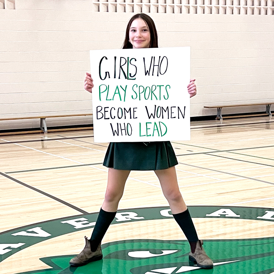 Girl holding up a sign that says "Girls who play sports become women who lead."