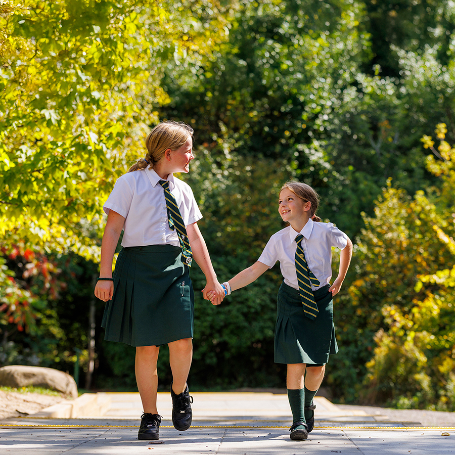 Two students holding hands and walking joyfully.
