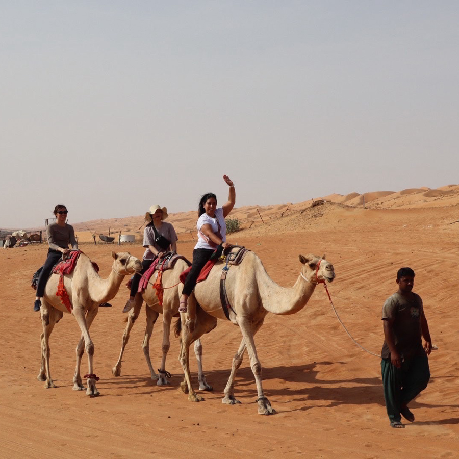 People riding on camels waving to the camera.